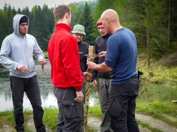 Gruppe arbeitet an einer selbstgebauten Konstruktion mit Holzstöcken am Ufer eines Gewässers