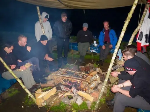 Gruppe sitzt um ein Feuer und bereitet Essen zu beim Survival Training
