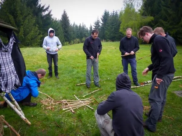 Gruppe von Personen arbeitet mit Ästen auf einer Wiese beim Überlebenstraining