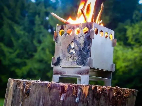 Hobo-Kocher mit Flamme auf einem Baumstumpf, umgeben von Bäumen