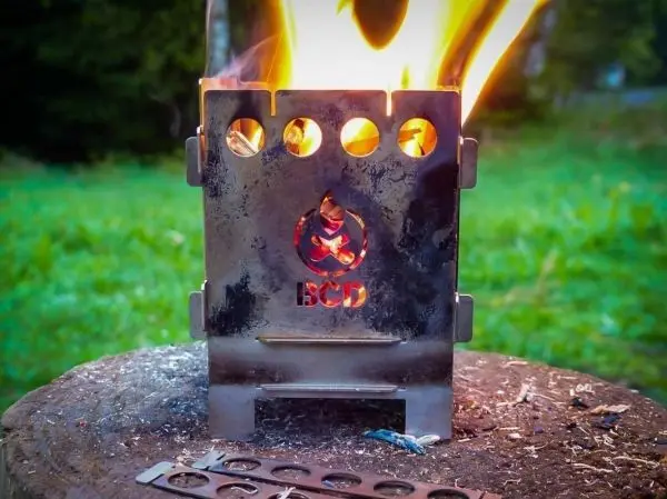 Hobo-Kocher mit Flamme auf einem Holzstück, daneben ein Metallstück