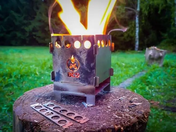 Hobo-Kocher mit Flamme auf Holzscheit, daneben Brennmaterial