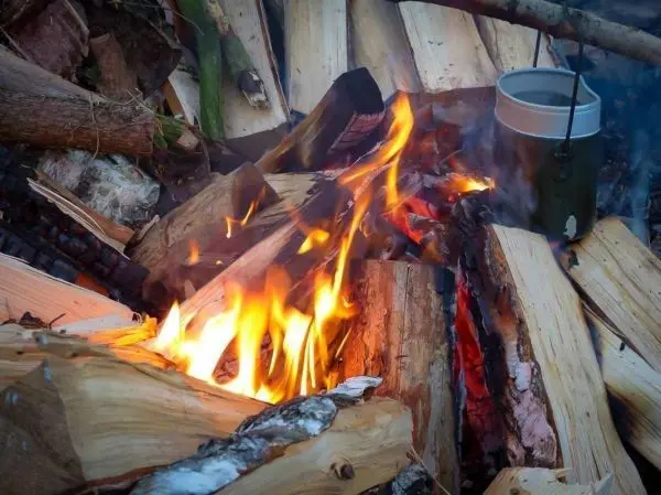 Kleine Flamme brennt zwischen Holzscheiten, Kessel hängt über dem Feuer