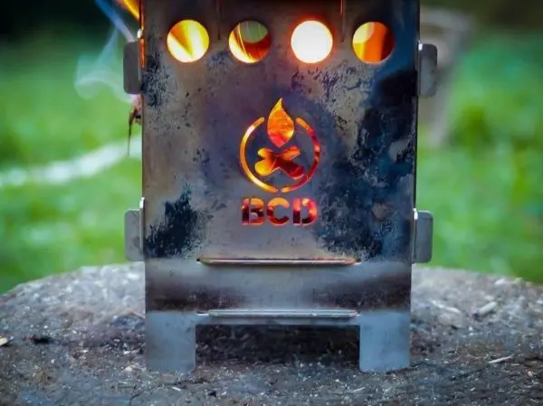 Kleine Flamme lodert aus einem Metallkocher auf einem Holzstück