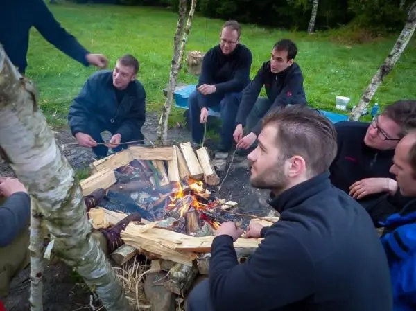 Kleines Bodenfeuer in einer Holzstruktur, Gruppe sitzt im Kreis darum herum