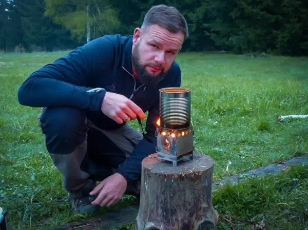 Kocher mit Dose auf Baumstumpf, Person entzündet Feuer mit Zunder