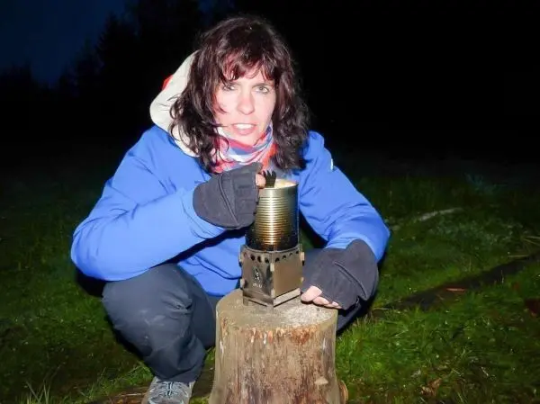 Kochgerät steht auf einem Baumstumpf, Person hält eine Dose darüber