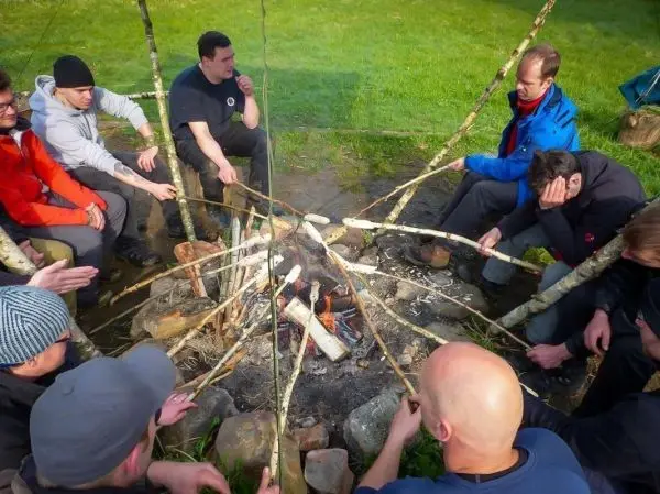 Kreis aus Personen um ein Feuer, Holzstücke brennen im Feuer