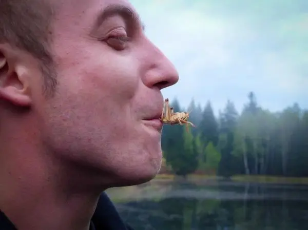 Mann hält eine Heuschrecke im Mund, während er am Wasser steht