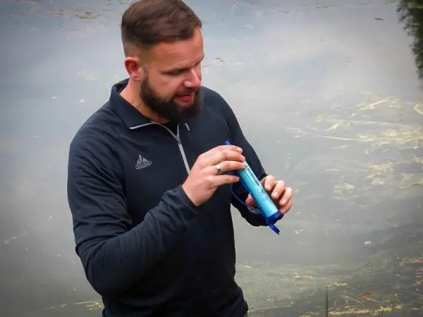 Mann hält einen Wasserfilter über einem Gewässer