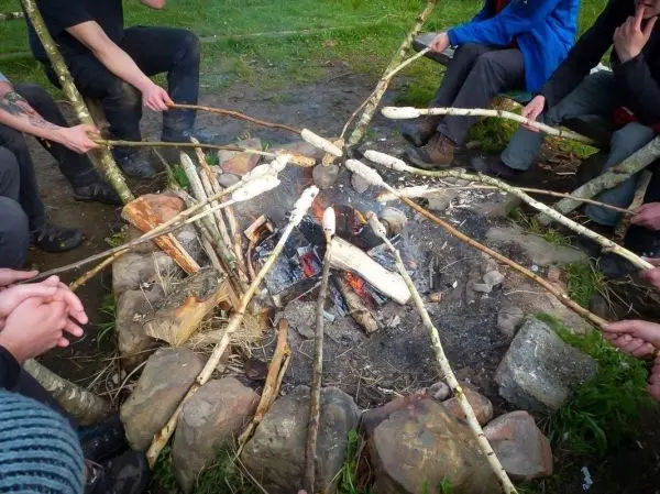 Mehrere Personen halten Stockspieße über ein Feuer beim Überlebenstraining