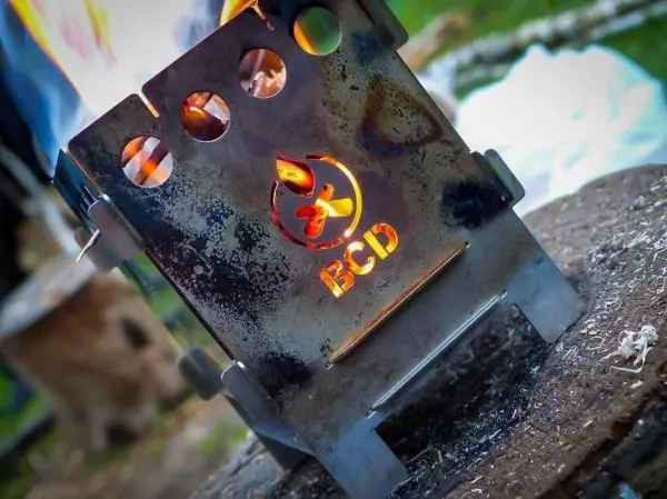 Metallkocher mit Flammen auf einem Holzstamm beim Kochen im Freien