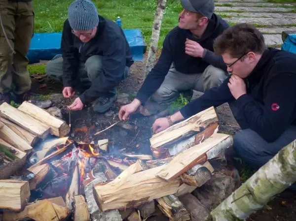 Personen fügen Holz zu einem Feuer hinzu beim Survival Training