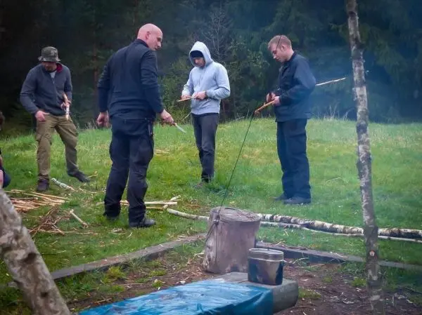 Vier Personen bearbeiten Holzstücke mit Messern in einer grünen Wiese