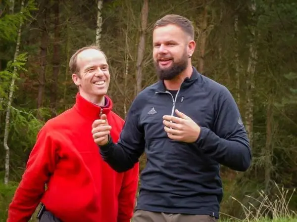 Zwei Männer stehen im Wald und unterhalten sich freundlich