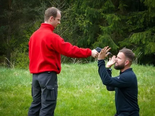 Zwei Personen interagieren im Freien, eine Person reicht der anderen ein Objekt