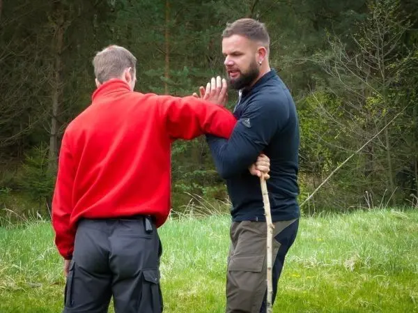 Zwei Personen üben eine Selbstverteidigungstechnik mit einem Stock im Freien