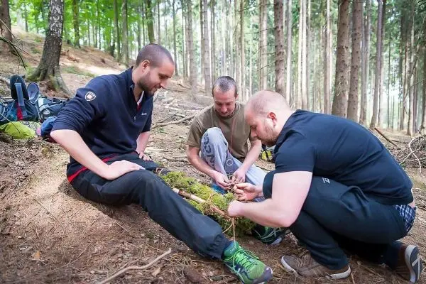 Drei Personen arbeiten am Boden im Wald an einer Holzstruktur