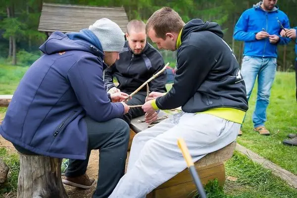Drei Personen arbeiten gemeinsam an einem Holzstück auf einer Bank