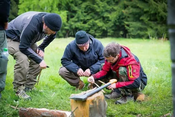 Drei Personen arbeiten gemeinsam an einer Holzarbeit mit einem Messer und einem Stock