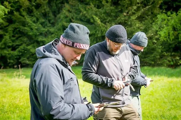 Drei Personen betrachten Karten in einer Wiese beim Überlebenstraining