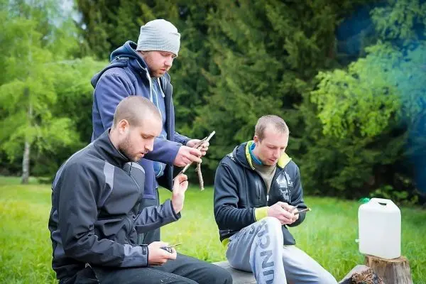 Drei Personen sitzen auf einem Baumstamm und nutzen Smartphones
