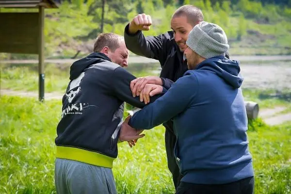 Drei Personen üben eine Selbstverteidigungstechnik im Freien