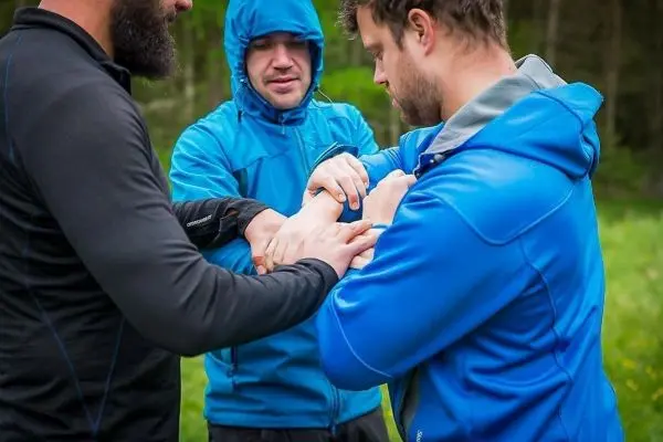 Drei Personen üben eine Technik zur ersten Hilfe am Arm eines Teilnehmers