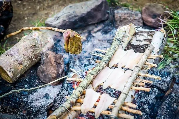 Fischfilets garen über einem offenen Feuer auf einem improvisierten Grill aus Ästen