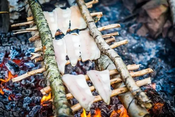 Fischfilets garen über einem offenen Feuer auf einer improvisierten Grillkonstruktion