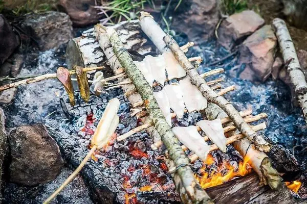 Fischfilets garen über einem offenen Feuer auf Holzstäben