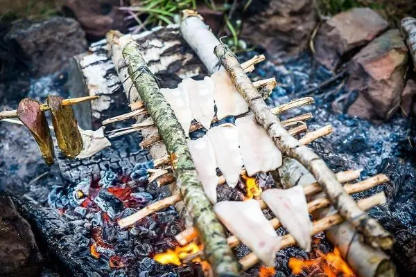 Fischstücke werden über einem offenen Feuer auf Holzstäben gegart