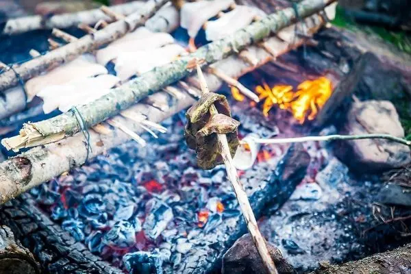 Fleischstück wird über einem offenen Feuer gegrillt beim Survival Training