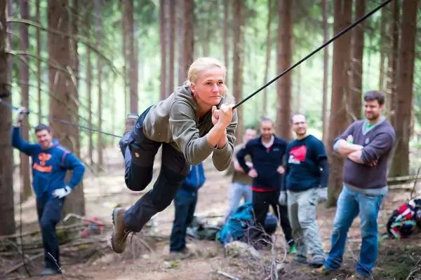 Frau überquert selbstgebaute Seilbrücke zwischen Bäumen im Wald