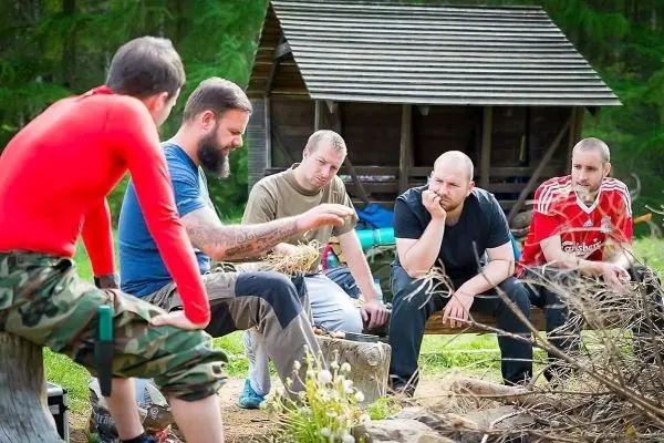Gruppe diskutiert am Lagerfeuer, Holzunterstand im Hintergrund