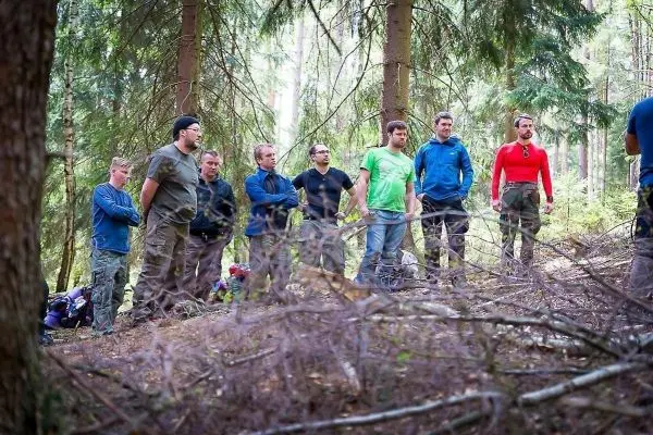 Gruppe von Personen hört einem Redner im Wald zu beim Überlebenstraining