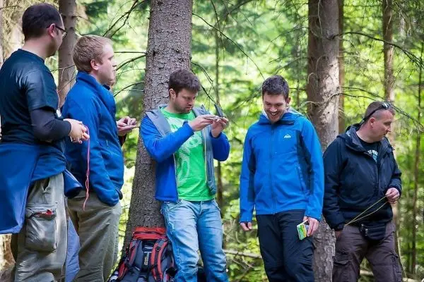 Gruppe von Personen steht an einem Baum im Wald und betrachtet Geräte