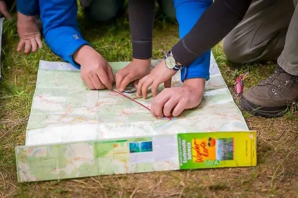 Hände legen einen Kompass auf eine Landkarte und ziehen eine Linie