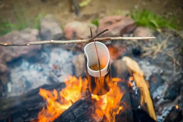 Kessel hängt über dem Feuer an einer improvisierten Halterung aus Ästen