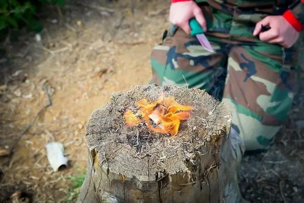 Kleine Flamme auf einem Baumstumpf, daneben ein Messer