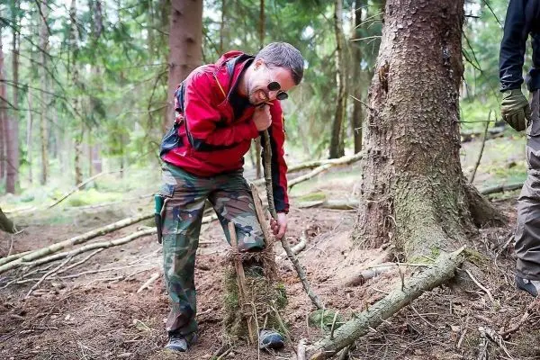 Mann baut eine Schlagfalle (Figure-Four-Falle) im Wald