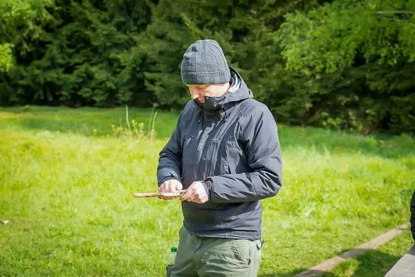 Mann bearbeitet einen Holzstock mit einem Messer im Freien