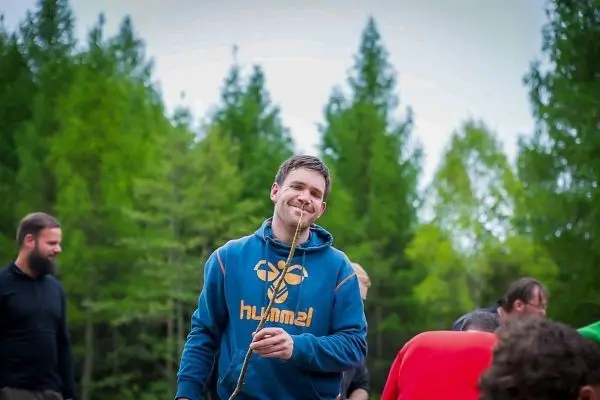 Mann hält einen Stock in der Hand und lächelt in einer Waldumgebung