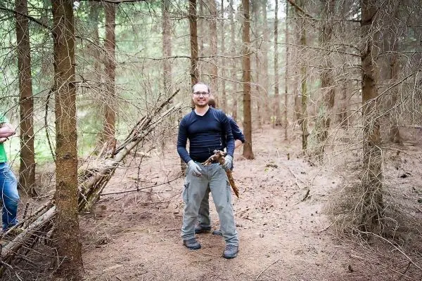 Mann hält einen Stock in einem Wald mit Nadelbäumen