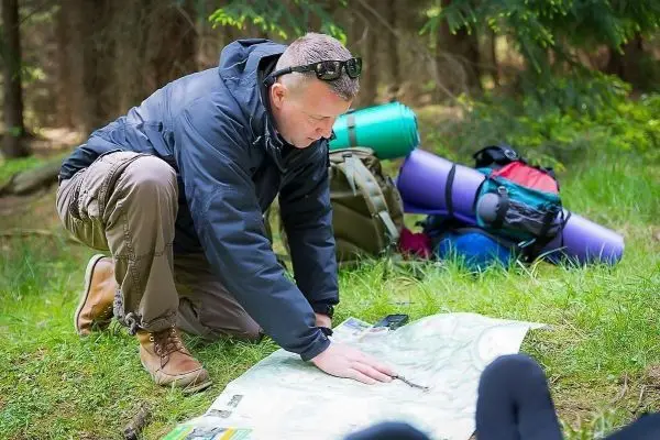 Mann kniet auf dem Boden und studiert eine Karte im Wald