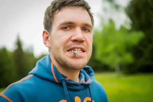 Mann mit einem Insekt im Mund steht in einer grünen Umgebung