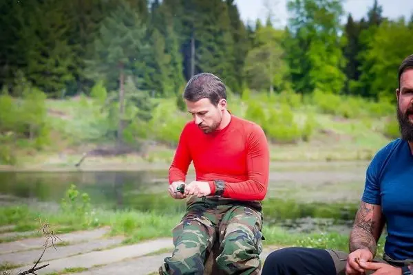 Mann mit Messer bearbeitet Holzstück am Ufer eines Gewässers