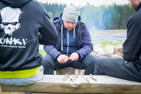 Mann schnitzt mit einem Messer an einem Holzstück auf einer Bank