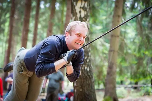 Mann überquert eine selbstgebaute Seilbrücke zwischen Bäumen