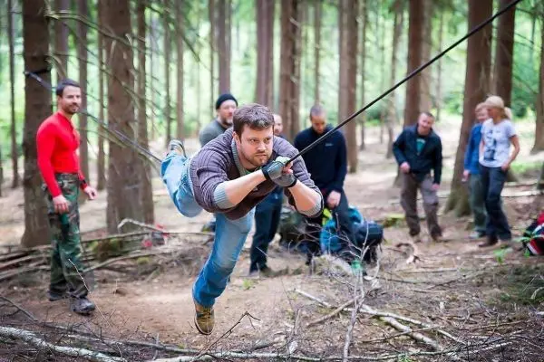Mann überquert selbstgebaute Seilbrücke zwischen Bäumen im Wald